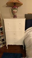Front view of white five-drawer tallboy dresser next to bed