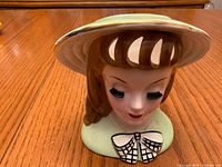 Front view of porcelain lady head vase showing hat, face, bow