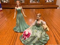 Front view of both Royal Doulton May Emerald figurines on wooden surface