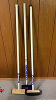 Front view of three curling brooms leaning against wood panel