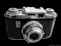 Front view showing camera body, lens, crest logo