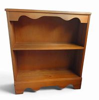 Front view of two-shelf wood bookcase showing scalloped trim