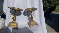Pair of brass candlesticks on white cloth background with clear view of bases and tops.