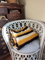 Folded crochet blanket draped on a white wicker chair, showing color pattern and texture.