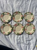 Set of six Franciscan Rose bread and butter plates laid out on fabric, showing floral design and scalloped edges.