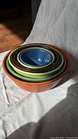 Top view of six Bauer nesting bowls stacked inside each other with orange bowl on the outside and smaller bowls inside showing multiple colors: brown, green, yellow, blue, dark purple.