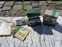 Overview photo showing several stacks and loose books including children's books, gardening books, and green hardcover set.