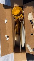 Top view of cardboard box containing vintage melamine plates and bowls, arranged in sections to prevent damage during transport or storage.
