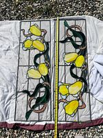 Full view of the two stained glass panels laid flat on a cloth, showing the yellow flowers, green leaves, and copper vines design with a measuring tape for size reference.