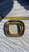 Stacked set of four square pottery baking dishes with a tape measure showing width approx 11 inches