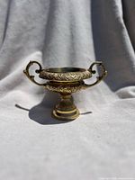Front view of vintage brass urn vase showing ornate handles and floral engravings.