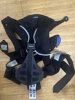 Photo of front side of Baby Bjorn baby carrier showing straps and mesh padding on wood surface