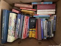 Top-down view of a box filled with various books including dictionaries, language learning materials, and reference guides tightly packed inside the box.