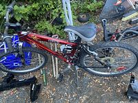 Side view of red Next boy's mountain bike leaning against a fence, showing frame, seat, pedals, and rear suspension coil spring.