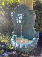 Front view of wall-mounted water fountain showing lion head spout with water flow and scalloped basin.
