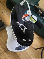 Full view of the 4moms MamaRoo infant swing seat with black fabric liner and dangling toys.