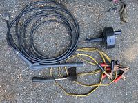 Wide shot showing jumper cables, auger blade, hatchet, and pressure washer hose coil on ground