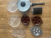 Photo of assorted kitchen items on wood surface showing glass plates, lidded soap dish, saucer molds, saucepan and flask