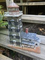 Front and side view of the metal lighthouse candle holder showing its weathered paint, windows, and balcony details.