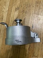 Side view of the cast aluminum hamburger press showing the lever and brand engraving 'our table'.