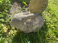 Side view of the grey concrete rabbit statue sitting on grass in a garden setting.