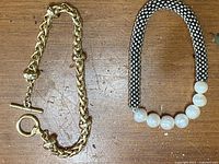 Two bracelets lying side by side on a wooden surface. One is a gold-tone chain bracelet and the other is a pearl bracelet with silver-tone beaded strands and large faux pearls.