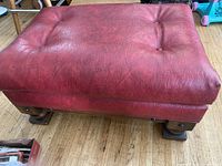 Side and top view of red ottoman showing tufted cushion and wooden legs.