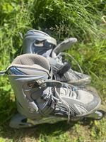 Side view of the grey inline rollerblades in grass, showing adjustable straps and padded ankle area.