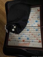 Folded open Scrabble game board with black fabric pouch containing letter tiles