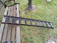 Steel motorcycle ramp shown outdoors on grass, placed diagonally across a bench to visualize size and features.