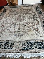Full view of the cream colored area rug showing intricate floral and scroll patterns and dark green border with medallions.