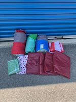 Outdoor photo showing rolled sleeping bags, folded flags, and folded tablecloths on pavement in front of a blue storage door.