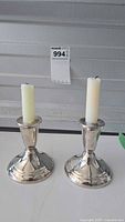 Pair of 4 inch silver candlesticks with white taper candles, shown from front angle on white surface, labeled with lot number.