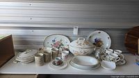 Wide view of all bone china items arranged on table including lidded serving bowl, platters, cups, and saucers