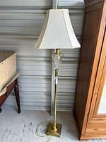 Full height view of the floor lamp showing brass stand, glass insert, and white shade next to furniture.