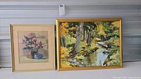Two framed artworks side by side including pastel floral drawing and autumn landscape painting