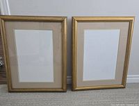 Two gold-colored picture frames side by side against a wall, showing neutral matte and blank white insert.