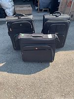 Front and side view showing three black wheeled suitcases, SwissGear in front and two other suitcases behind