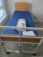Full view of the medical bed including the blue mattress, wood-effect head and footboards, and metal removable side rails attached on frame.