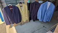 Four men's suit jackets displayed hanging inside a storage unit, showing various colors and styles.