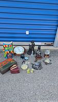 Overview of all items including clock, wooden boxes, large golfer and dog figures, whale figurines, alabaster bird and other small items arranged on concrete