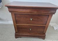 Front view of the wooden night table showing two drawers with metal keyhole escutcheons and crown molding on top.