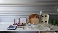 Overview of lot on table showing wooden cutting boards, porcelain tray, glass bowls, boxed steak knives and forks, and green glass serving piece.