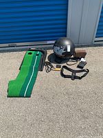 Lot overview showing golf putting mat, black helmet, analog scale, skipping rope, and bouncing ball.