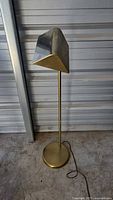 Full image of the standing floor lamp with brass base and metal angular shade, showing the lamp upright with electrical cord on the floor.