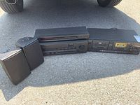 Full stereo system setup including tuner/amplifier, dual cassette deck, two speakers placed outside on pavement under natural light.