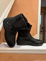 Side view of the motorcycle boots positioned sideways showing outer side and details including embossed logo and strap.