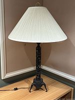 Full view of the antique-style table lamp showing the cream pleated shade and cast metal base on a wooden surface.