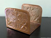 Front angle view of the copper bookend showing embossed floral design on both vertical sides and hammered texture base.