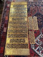 Overhead view of five gold-lacquered Burmese manuscript panels arranged on a patterned rug